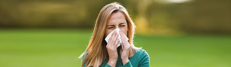 Women outside with blowing into a tissue from allergies and sinus issues