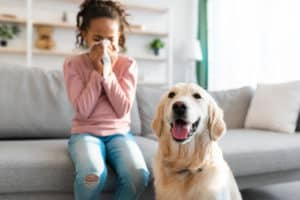 girl sneezing and holding paper napkin with a dog beside her