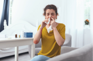 woman sitting on a grey couch using nasal spray for her runny nose