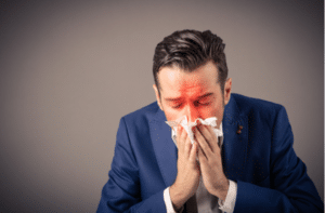 Sick businessman blowing nose in a tissue.