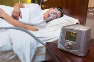 CPAP machine sitting on the table next to the bedside with sleeping man