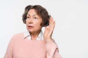 Close-up of senior woman touching her ear and leaning in to listen, illustrating hearing loss, curiosity, or active listening concept