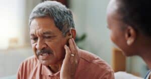 A nurse assists a man wearing a hearing aid, providing audiology support and medical care to improve hearing and wellness.