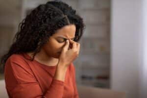 Young woman pressing the bridge of her nose with eyes closed, showing sinus pain, headache, and discomfort at home.